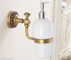 a white soap dispenser mounted on a wall next to a gold faucet