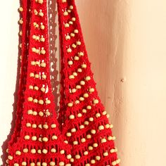 a red crocheted bag hanging from a hook on a wall with white beads