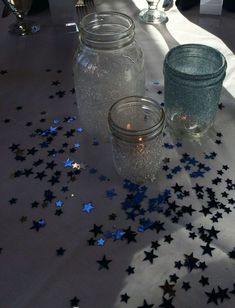 three mason jars sitting on top of a table covered in blue and silver glitter stars