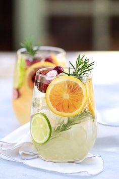 two glasses filled with white wine sangria and garnished with lemons, rosemary, cranberries, and orange slices