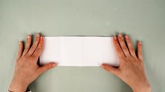 two hands holding an open white piece of paper on top of a gray surface with green walls