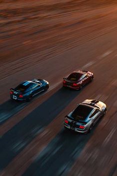 three cars driving down the road at sunset or sunrise, one is black and two are red