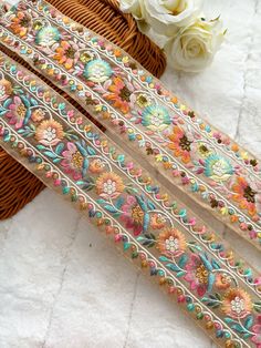 two ribbons with flowers on them sitting next to a basket and white rose bouquets