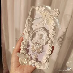 a hand holding a cell phone case with flowers and pearls on the back in front of a curtain