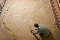 a man kneeling down on the floor in front of a circular wooden object that is being worked on