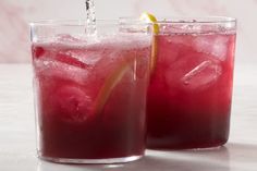 two glasses filled with red liquid and lemon wedged into the glass, one has an orange slice in it