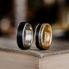 two gold and black wedding rings sitting on top of an open book with the pages folded down