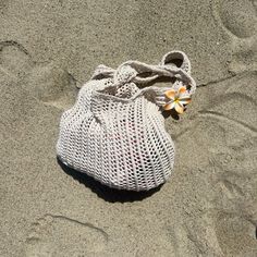 a white bag sitting on top of a sandy beach next to a small orange flower