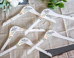 four wedding hangers with flowers on them sitting on a table next to greenery