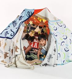 two children playing in a teepee tent made out of cloths and other fabric material