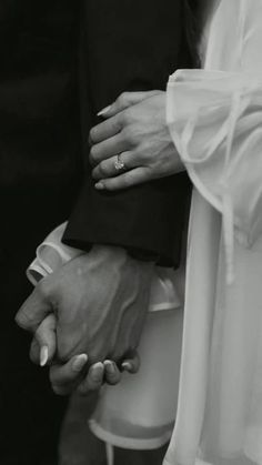 black and white photograph of bride and groom holding each other's hands with wedding rings on their fingers