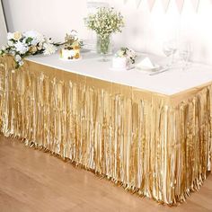 the table is covered with gold tinsel and white flowers in vases on it