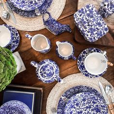 blue and white china is laid out on a wooden table with place settings, utensils, and plates