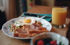 a breakfast plate with eggs, toast and fruit next to a glass of orange juice