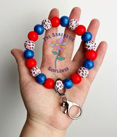 a hand holding a red, white and blue beaded bracelet with a flower charm