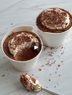 two bowls filled with chocolate desserts on top of a white counter next to a spoon