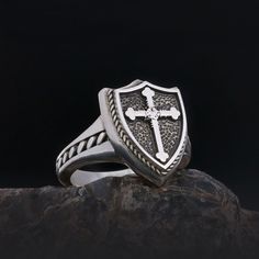 a silver ring with a cross on it sitting on top of a black stone slab