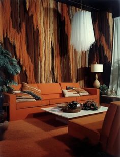 a living room with an orange couch and coffee table in front of a large wall hanging