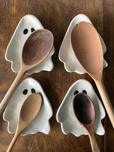 three spoons with faces on them are sitting in white dishes, one is shaped like a ghost and the other has a wooden spoon