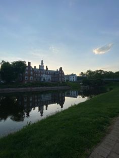 a large building sitting next to a body of water on top of a lush green field