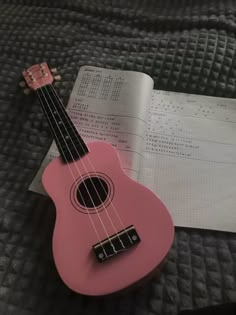 a pink ukulele sitting on top of a bed next to an open book