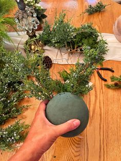 a hand holding a green ball with plants in it on a wooden table next to other decorations