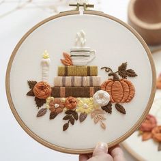 someone is holding up a embroidery project with pumpkins, books and flowers on it