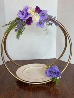 purple and white flowers are arranged in a circular metal stand on a wooden table top