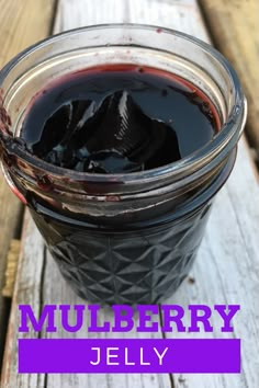 a jar filled with black liquid sitting on top of a wooden table next to a spoon