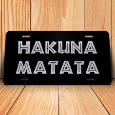 a black license plate with the words hakuna matata on it against a wooden background