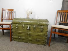 an old trunk sitting next to two wooden chairs