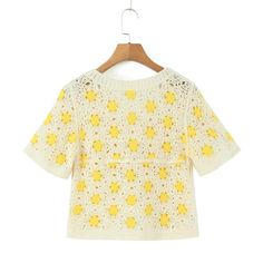 a white sweater with yellow flowers on it hanging from a wooden hanger in front of a