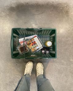 a person standing in front of a shopping basket with food and drinks on top of it