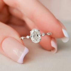 a woman's hand holding a ring with a diamond on it and white nail polish