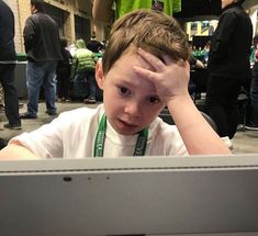 a young boy sitting in front of a computer monitor with his hand on his head