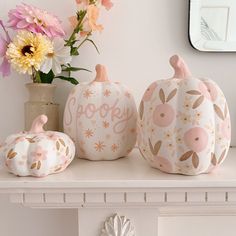 three painted pumpkins sitting on top of a white mantle next to a vase with flowers