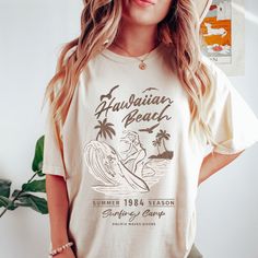 "Introducing our vintage-inspired beach tee by Comfort Colors! Made with premium quality cotton, this tee features a comfortable oversized fit and a washed-out, faded color palette that gives it a well-loved, lived-in look. The classic ribbed neckline and short sleeves make it the perfect choice for any casual outing, while the vintage-style print adds a touch of retro charm. Get ready to turn heads with this trendy and comfortable beach tee IMPORTANT:  Please read all details below! We want you to be completely happy with your purchase! 🌿 M A T E R I A L S This is an adult unisex COMFORT COLORS BRAND T SHIRT, IT IS 100% RING SPUN COTTON. 🌿 P R I N T I N G: Our shirts are made with Direct to garment printing, not vinyl! Which means your print will last longer and no peeling or cracking! Retro Surfing T-shirt For Beach Season, Retro Letter Print T-shirt For Beach Season, Retro Text Print T-shirt For Beach, Vintage Summer Beach T-shirt, Vintage Summer Tops With Custom Print, Vintage Custom Print Tops For Summer, Vintage Graphic Print Beach Shirt, Retro Cotton T-shirt For Beach, Retro Beach Season T-shirt