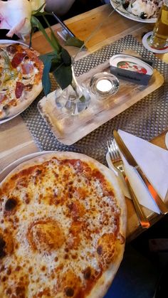 two pizzas are sitting on the table with silverware and flowers in vases