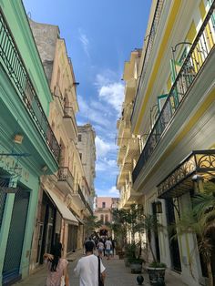 two people walking down an alley way with buildings on both sides and balconies above them