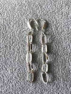 two pairs of silver chain earrings laying on the ground