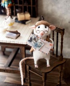 a stuffed mouse holding a piece of paper on top of a wooden chair in front of a table