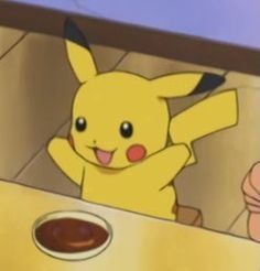 a pikachu sitting at a table in front of a plate of food with sauce on it