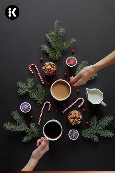 two hands holding cups of coffee with candy canes and candies on the table