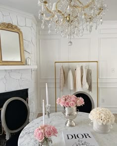 a white table topped with pink flowers next to a fire place and chandelier