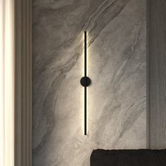 a wall mounted light on the side of a white and gray marbled wall next to a black chair