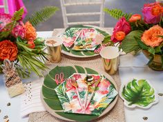 the table is set with plates, napkins and tropical flowers in vases next to each other