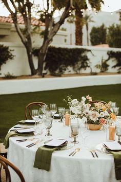 an outdoor table set with place settings and flowers in vases on the centerpiece