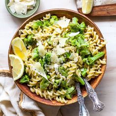 a bowl filled with pasta and broccoli on top of a table next to lemon wedges