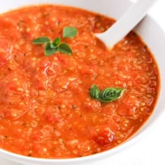 a white bowl filled with tomato soup and garnished with basil