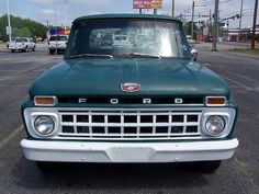 a green truck parked in a parking lot next to other cars and trucks on the street